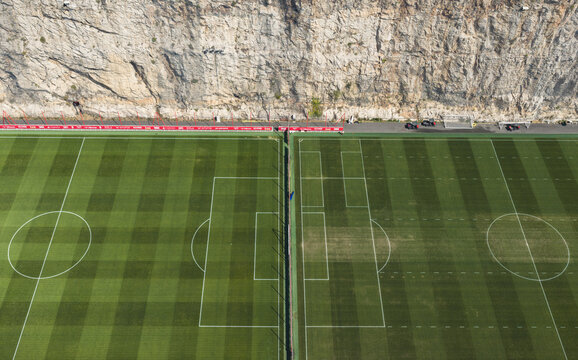 La Turbie, France - 16 August 2026: Aerial view of AS Monaco Performance Center with adjacent football pitches, geometric field markings, contrasting grass patterns, and a limestone cliff.