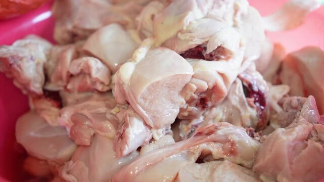 Fresh raw chicken pieces piled in a pink plastic bowl ready for cooking. Close-up shot highlights texture and natural color of unprocessed poultry meat, elegantly showcasing preparation.