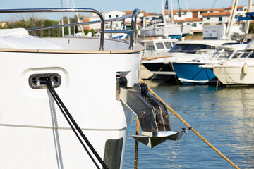 White yacht anchored at marina with visible bow, anchor, and mooring lines, surrounded by various boats and clear blue water in the background © Vlad Yakubovskiy
