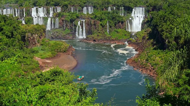 Aerial view of waterfalls with a small tourist boat on the river surrounded by lush tropical rainforest