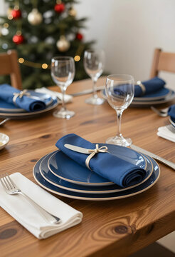 Holiday dinner table setting with blue plates and festive christmas tree in background, celebration and gathering
