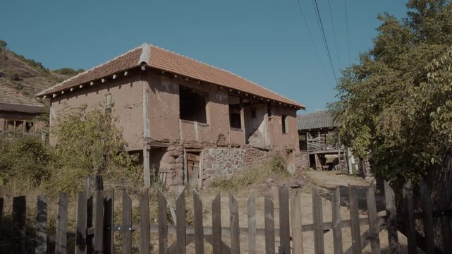 Camera pulling back to reveal an old traditional mud brick house behind a wooden picket fence in Topli Do village, Stara Planina, Serbia. Authentic Balkan rural architecture shot.