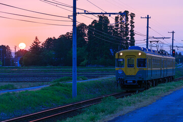 Obraz premium 日没間近の太陽が輝かせる線路を富山地方鉄道の愛称「かぼちゃ電車」が走る