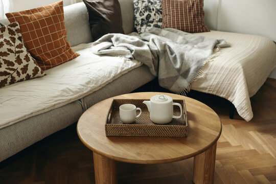 Cozy Living Room Scene with Round Wooden Coffee Table and Teapot Set on tray. Blurred background with sofa, wool plaid, cushions. Autumn Halloween Thanksgiving home decor. Elegant Interior. Breakfast