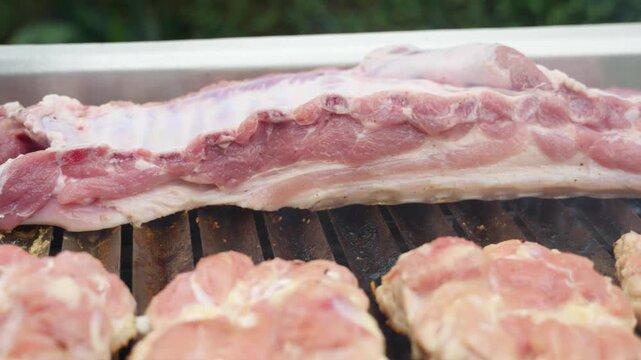 Raw pork ribs and meat grilling on hot barbecue