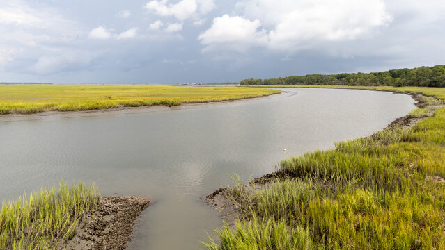 Drone view shows a curve of the river through marshland under cloudy sky near coastal area