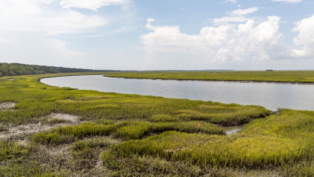 Drone captures aerial view of river winding through marshland with green vegetation under blue sky