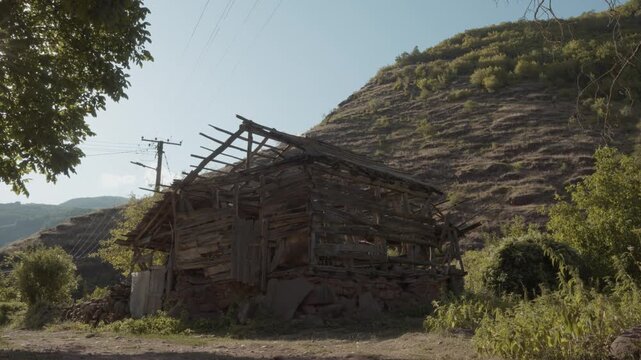 Abandoned and ruined old wooden barn with a collapsed roof structure set against a rocky mountain hill in Topli Do village, Stara Planina, Serbia. Authentic rural decay footage.