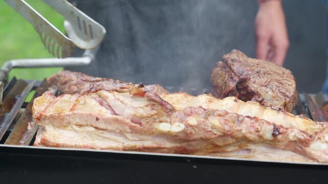 Chef grilling juicy pork ribs and beef steak on barbecue