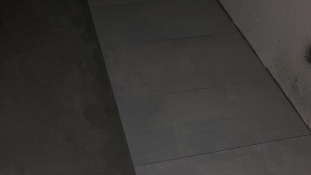 Gray floor tiles installed along unfinished concrete wall