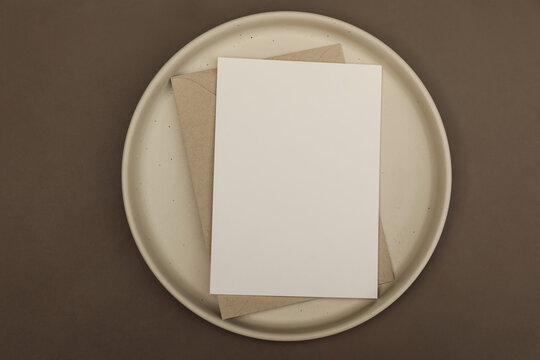 Blank White Greeting card Invitation Mockup with Craft Envelope, Spotted Ceramic Plate. Brow textured table background. Elegant wedding invitation, branding stationery. Flat lay, Top View, copy space