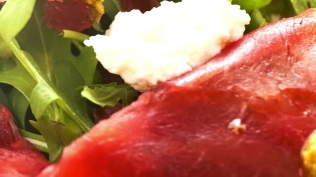 Close-up of fresh green arugula salad with red meat and white cheese.