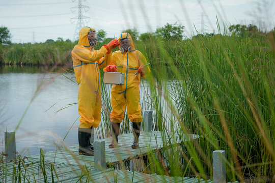 Protective suit respirator technician water sample wetland marsh dock pollution safety team conduct environmental contamination research beside marsh water using field equipment and caution
