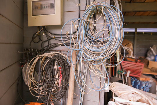 Bundle of electrical cables and wiring hanging in mess. Disorganized cabling in garage workshop or utility room. Untidy storage of power cord.