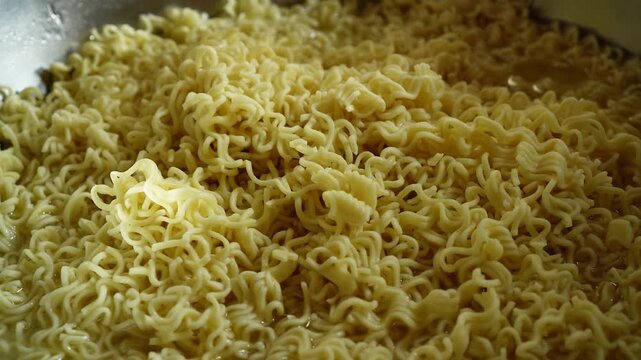 Close-up of cooked instant noodles in a bowl with a spoon resting beside them. Golden yellow strands soaked in broth, ready to eat. Simple, warm, comforting meal.