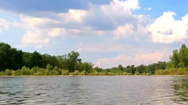 Scenic view of a tranquil river flowing past green trees under a cloudy blue sky