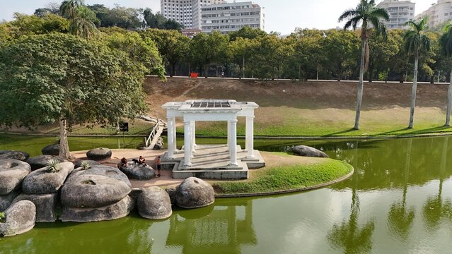 Aerial view of a white pavilion on a small island in a pond at Quinta da Boa Vista surrounded by lush trees, large rocks, and a grassy bank in Rio de Janeiro, Rio de Janeiro, Brazil.