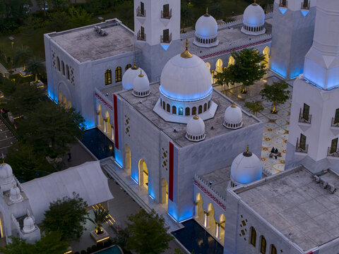 Aerial view of Sheikh Zayed Grand Mosque Surakarta with its white domes, intricate architectural details, and blue ambient lighting at dusk in Kecamatan Banjarsari, Jawa Tengah, Indonesia.