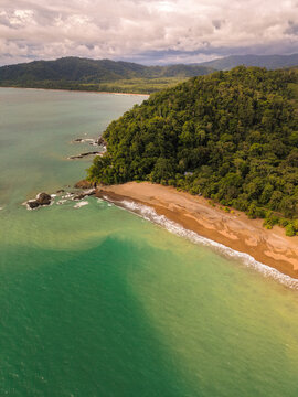 Aerial view of Drake Bay featuring a pristine sandy beach bordered by dense tropical rainforest and rocky coastal formations meeting the turquoise waters of the Pacific Ocean in Costa Rica.