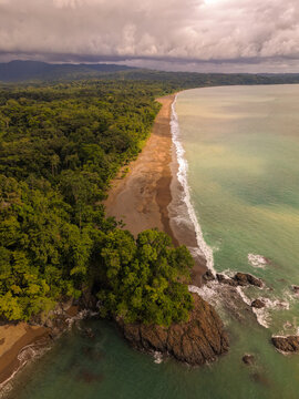 Aerial view of Drake Bay featuring a sandy coastline bordered by dense tropical rainforest and rocky cliffs meeting the turquoise ocean in Costa Rica.