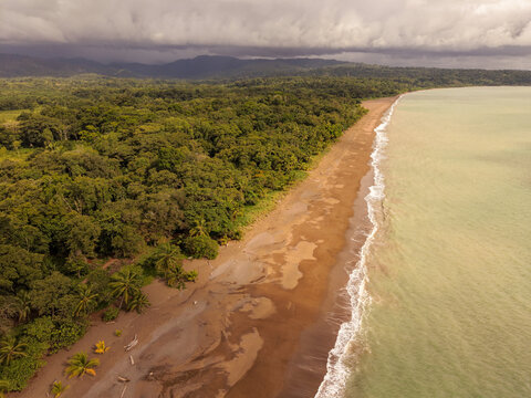 Aerial view of Drake Bay coastline featuring a sandy beach bordered by dense tropical rainforest and gentle ocean waves in Costa Rica.