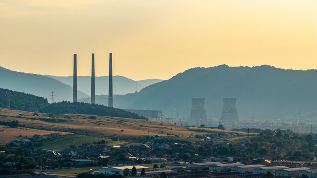 Aerial view of Mintia Power Station with its prominent cooling towers and chimneys set against rolling hills and a golden sunset sky in Deva, Hunedoara, Romania.
