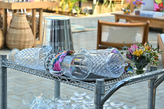 outdoor drink cart service with glassware next to coconut palm tree, beach event reception setup with tropical background, welcome drink station for coastal wedding or party