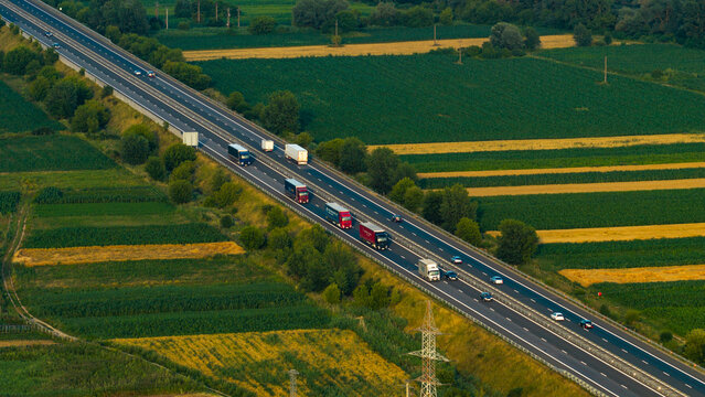 Aerial view of a highway with trucks and cars driving through agricultural fields and green landscape in Deva, Hunedoara, Romania.