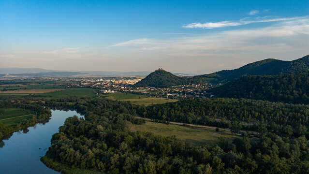 Aerial view of Deva Citadel perched on a hill overlooking the city, with a winding river, lush green forests, and surrounding fields in Deva, Hunedoara, Romania.