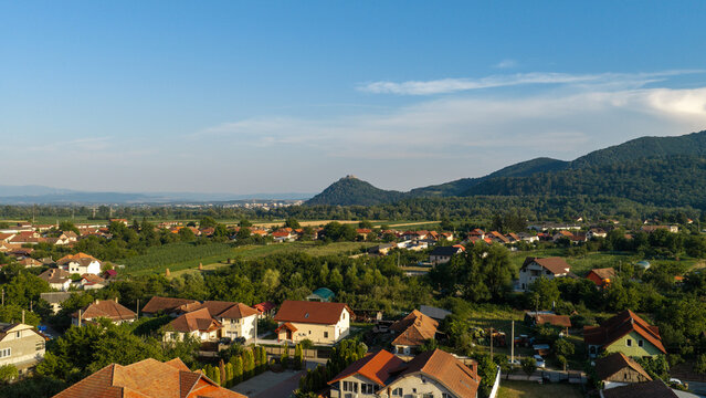 Aerial view of Deva Fortress perched on a hill overlooking the town of Deva with lush green trees, residential houses, and rolling hills in Deva, Hunedoara, Romania.