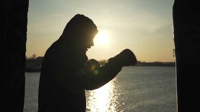 Silhouette of a Boxer Training with a Punching Bag at Sunset