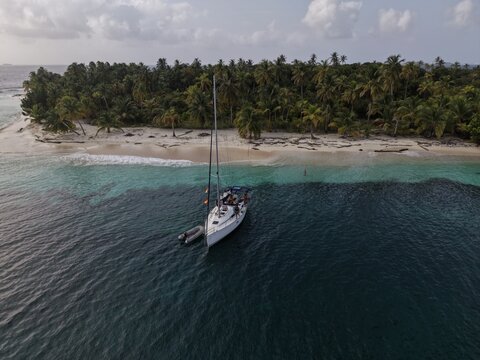 Aerial view of a sailboat anchored in the turquoise waters off a tropical island with a white sand beach and dense palm trees, Guna Yala Comarca, Panama.