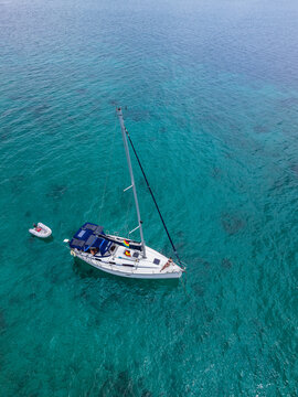 Aerial view of a sailboat anchored in the clear turquoise waters with a small dinghy attached and a woman relaxing on the deck in Guna Yala Comarca, Panama.