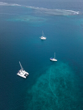 Aerial view of three sailboats floating in the clear turquoise waters of the Caribbean Sea near the coral reefs of Guna Yala Comarca, Panama.