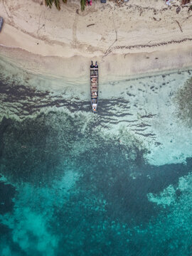 Aerial view of a long wooden boat moored on the sandy shore of a tropical beach with clear turquoise water and coral reefs in Guna Yala Comarca, Panama.