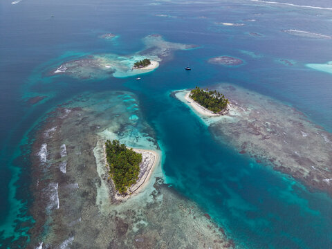 Aerial view of tropical islands with lush palm trees and white sand beaches surrounded by vibrant coral reefs and turquoise Caribbean waters in Guna Yala Comarca, Panama.