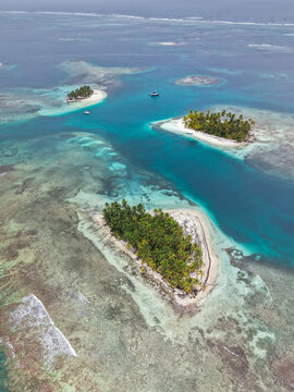 Aerial view of tropical islands with lush palm trees surrounded by turquoise water and coral reefs in Guna Yala Comarca, Panama.