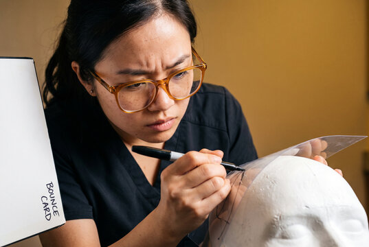Focused makeup artist sketching a face chart on mannequin head
