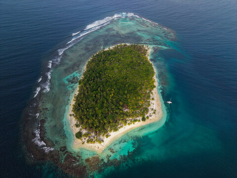 Aerial view of a lush tropical island surrounded by turquoise waters, a coral reef, and white sand beaches in Guna Yala Comarca, Panama.