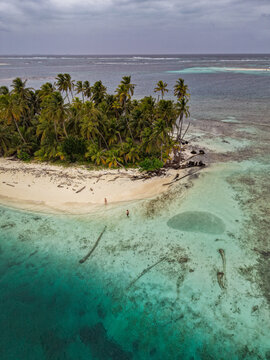 Aerial view of Guna Yala Comarca featuring a tropical island with palm trees, white sand beach, and turquoise waters with two people on the shore Guna Yala Comarca, Panama.