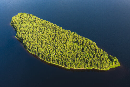 Aerial view of Siljan lake featuring a small, lush green island covered in dense pine forest surrounded by deep blue water in Mora, Dalarna County, Sweden.