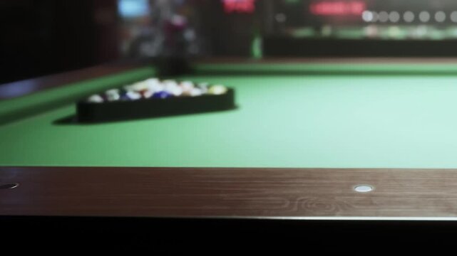 A group of people enjoys a game of pool in a busy bar. The green felt billiards table is filled with colorful balls. The atmosphere is lively during the evening.