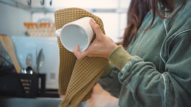 Close-up of an anonymous woman's hands drying a cup in her kitchen, showing a simple household task during a routine moment at home.
