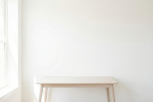 Minimalist wooden desk against blank white wall with natural window light