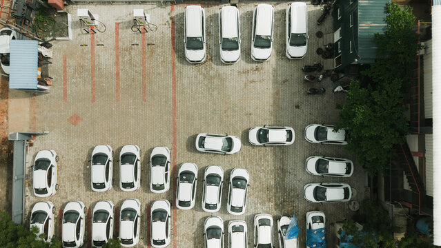 Aerial view of an EV charging station in a parking lot filled with white cars, featuring paved ground and charging infrastructure in India.