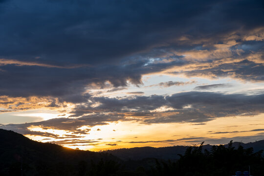 Golden light breaking through dramatic clouds at sunset, illuminating rolling hills and creating a serene, picturesque landscape with warm and cool tones