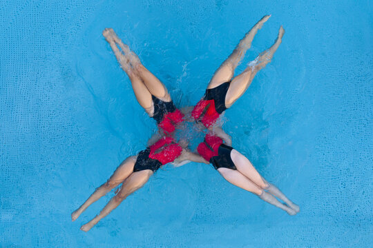Mulhouse, France - 10 August 2026: Aerial view of synchronized swimmers forming a star pattern in the blue water of the Stade Nautique pool.