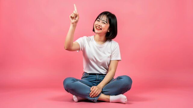 Idea Lightbulb Moment: A young woman with a joyful expression sits cross-legged, pointing upwards with an index finger, signifying a moment of inspiration or a great idea.
