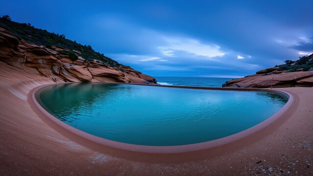 Serene natural landscape featuring a kidney-shaped pool of turquoise water surrounded by reddish-brown rocky formations and lush greenery under a cloudy sky