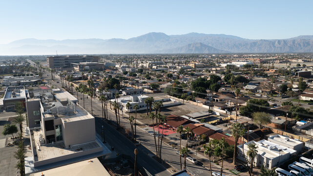 Indio, California, United States - 24 December 2023: Aerial view of a suburban landscape with palm trees, low-rise buildings, and distant mountains under a clear sky.